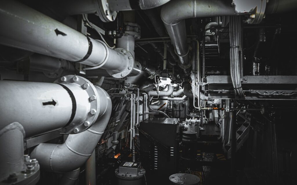 Large-bore intake and exhaust piping inside a commercial ship engine room, showing the scale of air management systems requiring filtration in Gulf operating conditions.