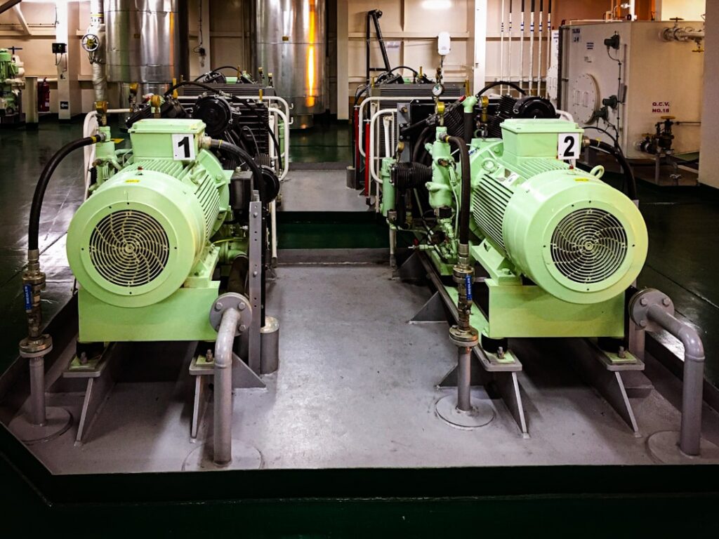 Two numbered green auxiliary generator motor units mounted on a ship's engine room deck